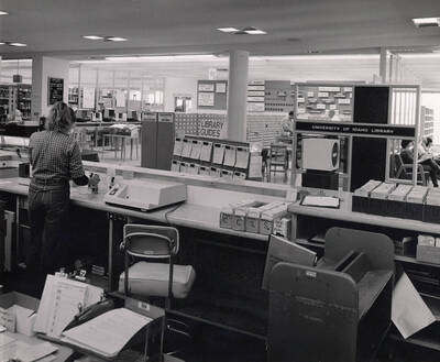 October 1, 1982 photograph of the Library. A library employee mans the loan desk with a card catalog in the background.