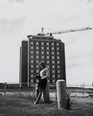 1969 photograph of the Donald R Theophilus Residence Hall under construction. A student reads a book in foreground. Donor: Publications Dept.