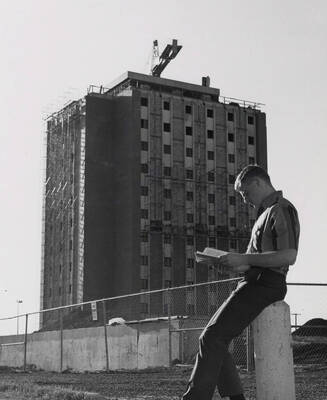 1969 photograph of the Donald R Theophilus Residence Hall under construction. A student reads a book in foreground. Donor: Photo Center.