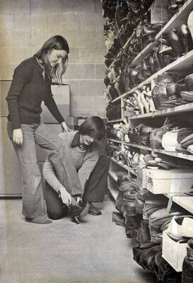 1975 photograph of Hartung Theatre. Students try on shoes in the costume storage area.