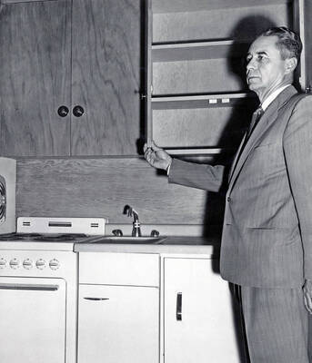 1957 photograph of the Park Village Apartments. Warner Cornish Jr., Director of Family Housing inspects a kitchen. Donor: Publications Dept.