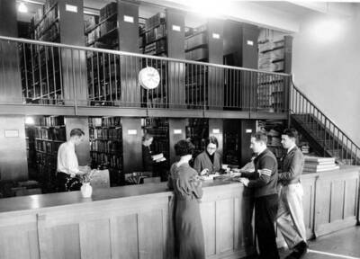 1936 photograph of the Library. Students receive help from librarians at the loan desk.