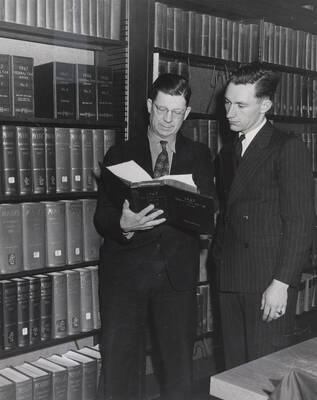 1947 photograph of the Law Library. Two men look through a book. Donor: Publications Dept.