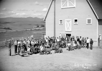 1939 photograph of sheep on the University of Idaho campus. Students pose with sheep outside of a barn.