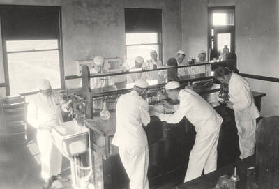 1925 photograph of Dairy Farm and Creamery. Students work at a lab table in the Creamery.