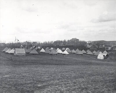 1910 photograph of Military Science Cadets. Tent encampment. University buildings in background.