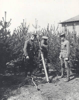 1914 photograph of Military Science Cadets. Military cadets loading a mortar surrounded by young pines.