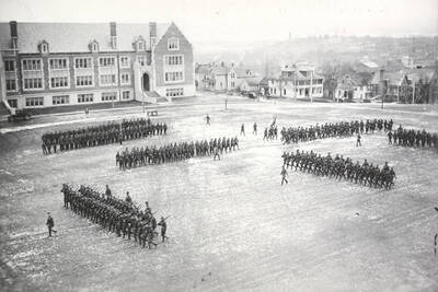 1925 photograph of Military Science Cadets. Military cadets on parade in front of the Science Hall with campus buildings in the background.