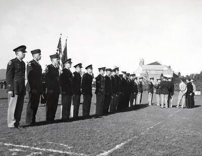 1953 photograph of Military Science Cadets. Cadet receiving an award at MacLean Field. Campus buildings visible in the background.