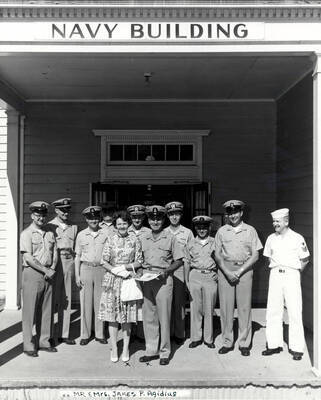 1962 photograph of Naval Science. Naval Science staffs stands in front of the Navy Building. Mr. And Mrs. James P. Agidius at front. Donor: Publications Dept..
