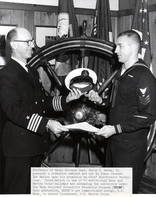 1964 photograph of Naval Science. Capt. Harry E. Davey presents promotion warrant and hat to student Bob Maisch. Donor: Publications Dept.