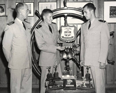 1964 photograph of Naval Science. Cadets receive admiral's reward l-r: Capt. Harry E. Davey, Kris A. Kirkland, Lee Roy Brannan. Donor: Publications Dept.