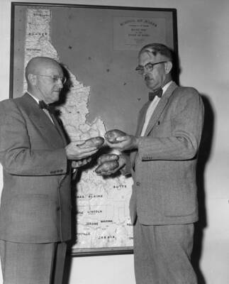 1954 photograph of Plant Sciences. George Woodbury shows potatoes to Dr. Theophilus in front of a map of Idaho. Donor: Publications Dept.