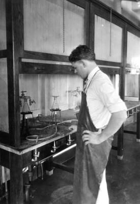 1935 photograph of Chemistry Class. Student working at a lab hood in the chemistry lab.