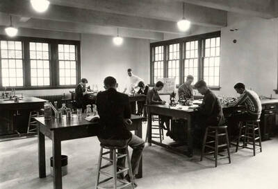 1933 photograph of Bacteriology building. Students work at their workstations in the lab.