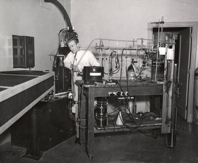 1952 photograph of Physics building. Student works with lab equipment.