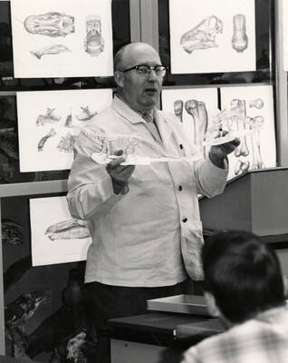 1965 photograph of Zoology building. Professor holds a small skeleton while giving a lecture.