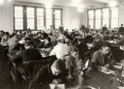 1938 photograph of Botany building. Students work with microscopes in the lab.