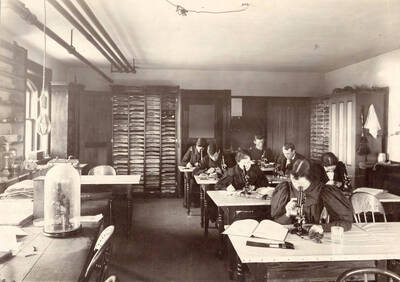 1896 photograph of Botany building. Students work with specimens at their workstations.