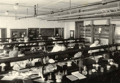 1928 photograph of Agricultural chemistry building. Students work with equipment at lab workstations.