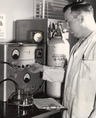 1959 photograph of Agricultural chemistry building. Professor adjusts equipment.