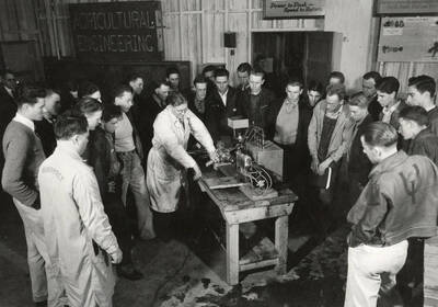 1928 photograph of Agricultural engineering building. Professor demonstrates the equipment to students in the shop.