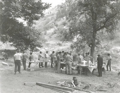 1968 photograph of College of Forestry. Students gather around tables near a campfire during the forestry summer camp. Also print. Donor: Fred Johnson.