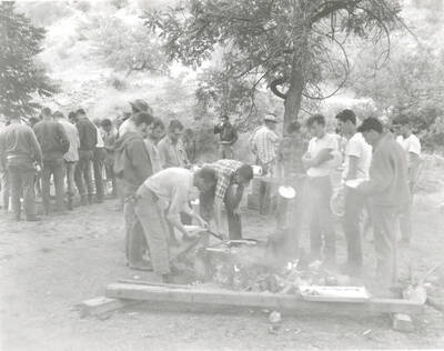1968 photograph of College of Forestry. Students gather around a campfire during the forestry summer camp. Also print. Donor: Fred Johnson.