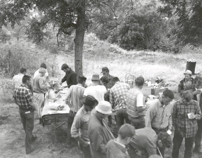 1969 photograph of College of Forestry. Students gather around tables at the campsite during the forestry summer camp. Also print. Donor: Fred Johnson.