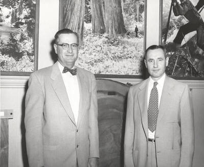 1953 photograph of College of Forestry. President Buchanan with the new Forestry Dean Ernest Wohletz stand in front of photographs of forestry scenes.