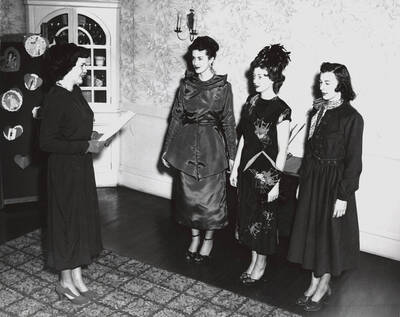 1952 photograph of Home Economics. Three students modeling dresses talking to a commentator during a fashion show.