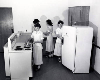 1955 photograph of Home Economics. Jan Morgan, Barbara Pierce, and two unidentified students work in a kitchen laboratory. Donor: Publications Dept.