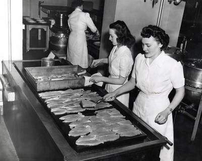 1955 photograph of Home Economics. Students cooking on a large griddle during class. Donor: Publications Dept.