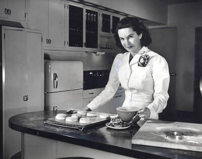 1955 photograph of Home Economics. A student shows a tray of english muffins. Donor: Publications Dept.