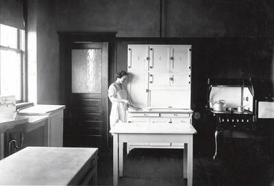 1928 photograph of Home Economics. A student in the Home Economics unit kitchen.