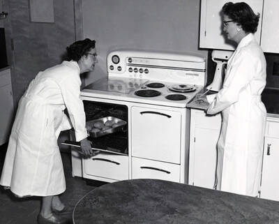 1955 photograph of Home Economics. Mary Zaehringer (right) and an unidentified woman bake Idaho potatoes in the Home Economics kitchen. Donor: Publications Dept.