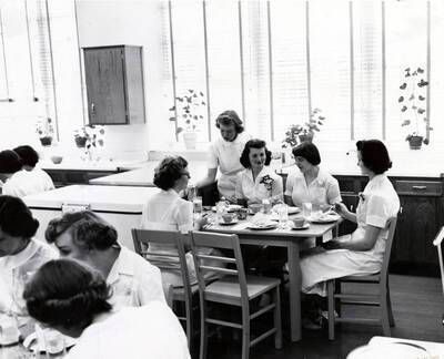 1952 photograph of Home Economics. Students eating at tables during cooking class. Donor: Publications Dept.