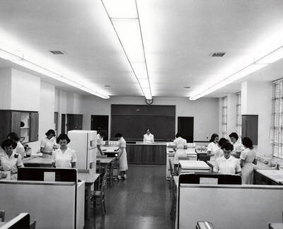 1952 photograph of Home Economics. Students working in the Home Economics cooking laboratory.