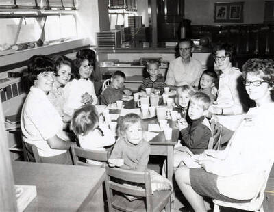 1956 photograph of Home Economics. Janice Hulsizer, Joyce Detchman, Fran Park, Vance Youmans, Ned Warnick (turned four), Mrs. Calvin Warnick, Brad Rabe, LaDessa Smelcher, Carolyn Helton, Eric Anderson, Betty Corbett, Tanys Steele, and Vicky Kappler sitting around a table during a birthday party.