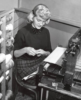 1960 photograph of Home Economics. A student threading a loom during weaving class.
