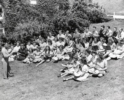 1944 photograph of Music Department. Summer school choral group rehearses outside in front of the Music building.