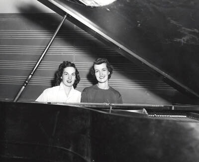 1954 photograph of Music Department. Phyllis Grocke and Jane Bostic sitting at a piano in front of a blackboard.