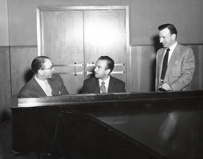 1950 photograph of Music Department. Hall Macklin, Glen Lockery and an unidentified man sit behind a piano. Donor: Publications Dept.
