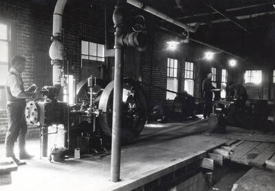 1936 photograph of College of Engineering. A student turns a valve on a steam engine.