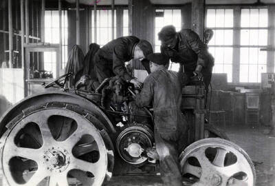 1933 photograph of College of Engineering. Students work on a tractor during class.