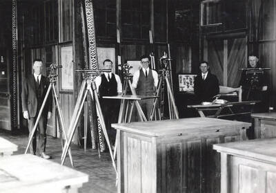 1922 photograph of College of Engineering. Students standing behind their surveying equipment in the drafting room.