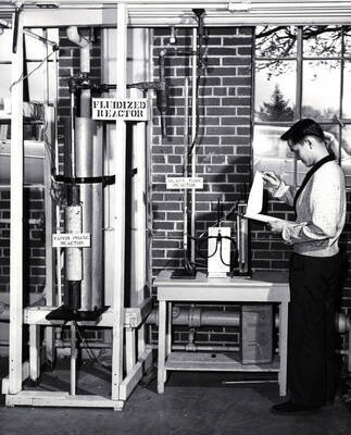 1956 photograph of College of Engineering. Fernando Vincente reading from a clipboard next to a fluidized reactor. Donor: Publications Dept.