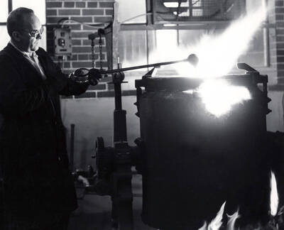 1962 photograph of College of Engineering. Assistant Professor Harolds Amos checking the temperature of aluminum alloy.