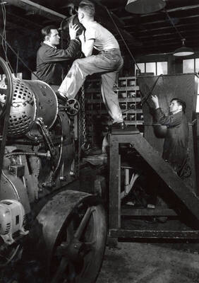 1940 photograph of College of Engineering. Students adjusting heavy equipment in a mechanical lab.