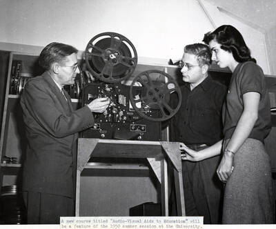 1950 photograph of Audio Visual Aids Service. Professor Allan Perry threading film in a projector. Donor: Publications Dept.